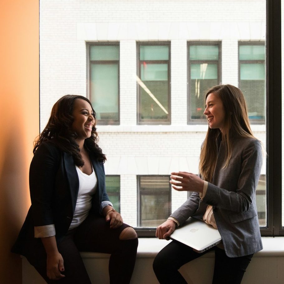 Skill Loop Collective Service Page Two women sit by a window, engaged in a friendly conversation.